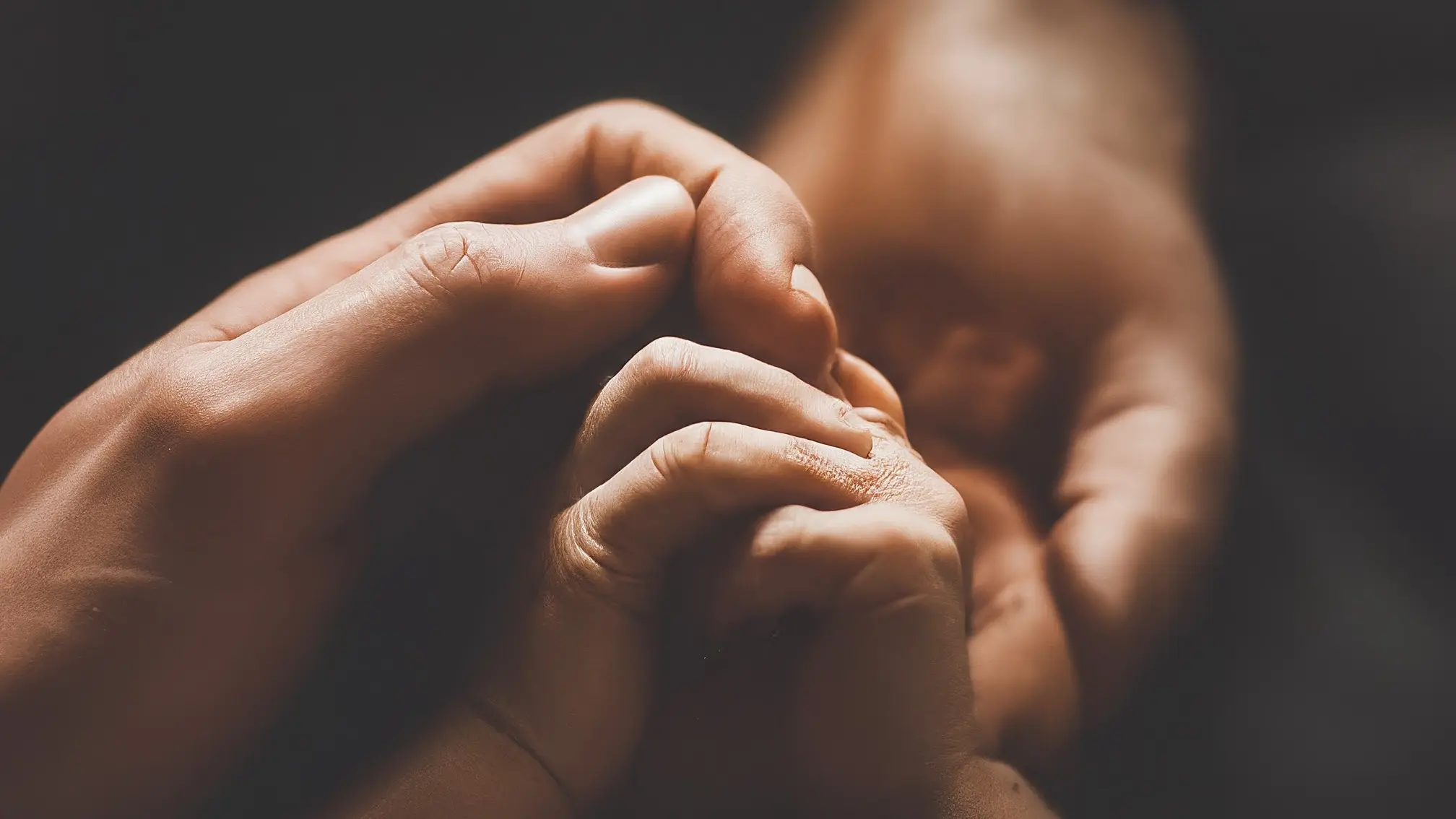 Una mano adulta sosteniendo suavemente la mano de un bebé, rodeadas por una cálida luz dorada.